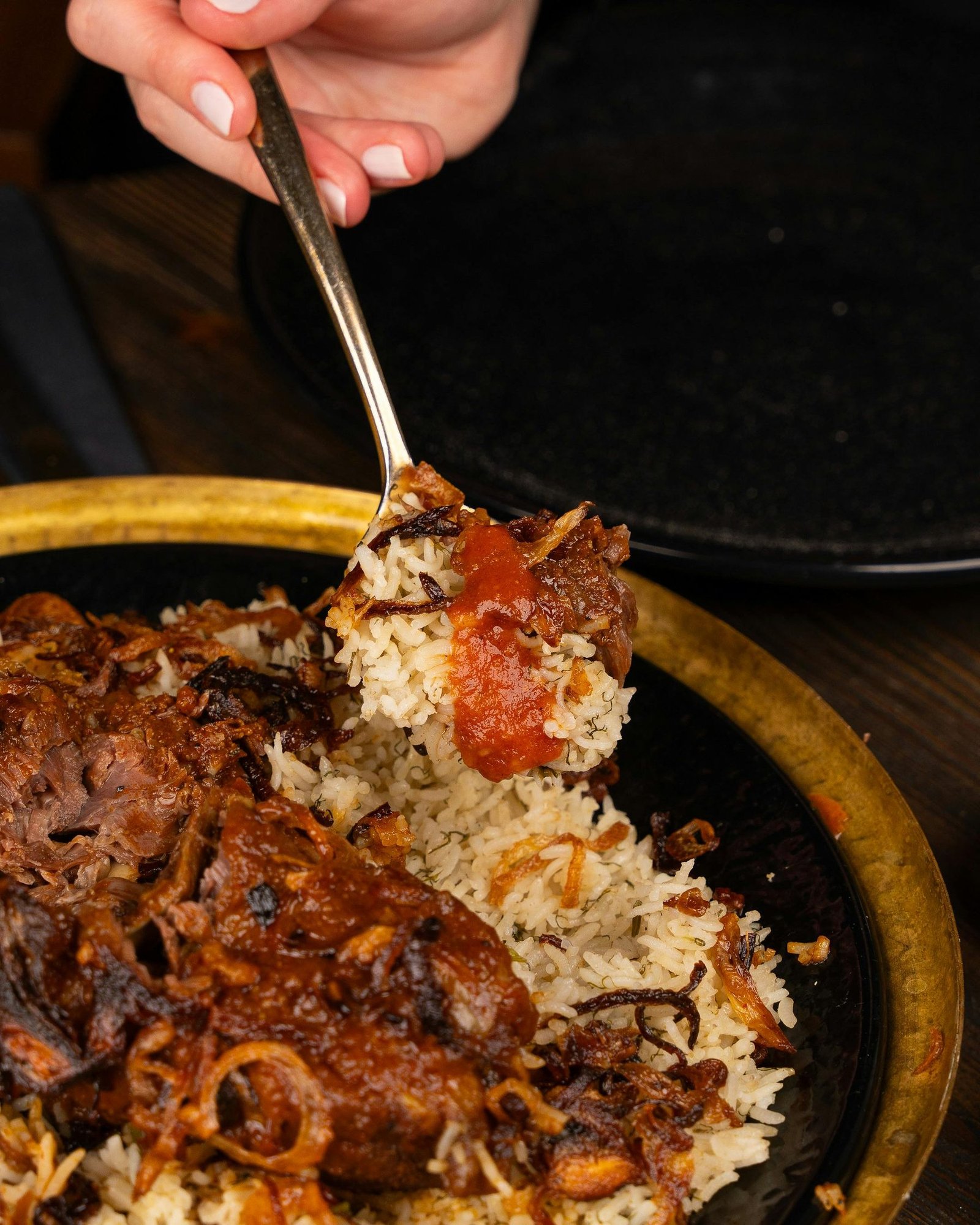 Close-up of a spoon lifting fragrant Arabic rice with caramelised onions and tomato sauce