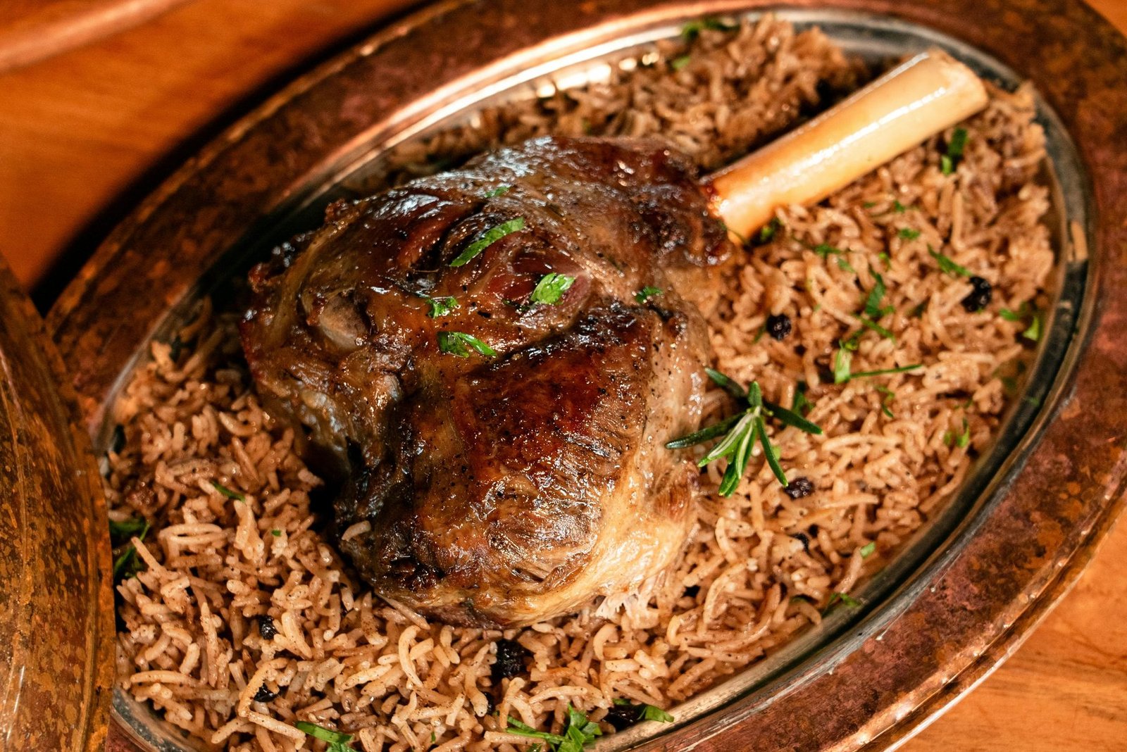 Roasted lamb shank close-up on a copper Arabic platter with herb-flecked rice and pomegranate seeds